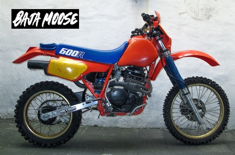 Very clean red 1986 Honda XR600R dirt bike with blue seat, leaning against a wall