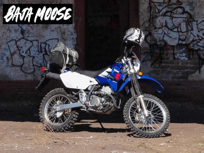 Blue Suzuki DRZ400S dual-sport motorcycle parked in front of a graffiti covered wall